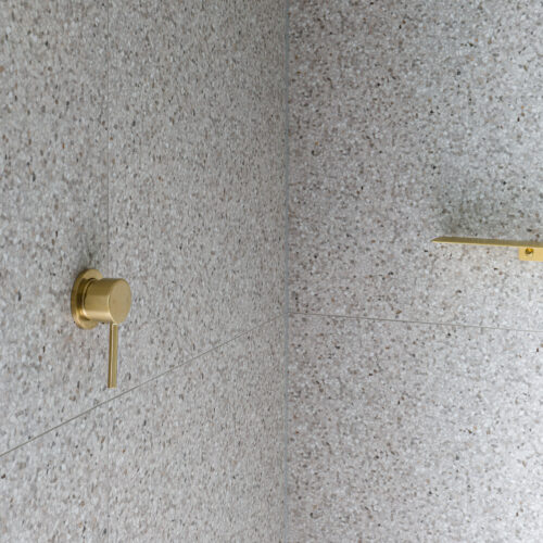 Brushed brass shower shelf and wall mixer on terrazzo tiles