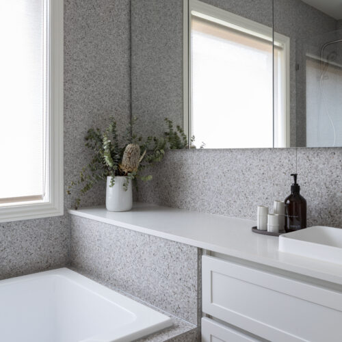 Built in bath with grey tile against a custom vanity unit with shaker style drawers in white