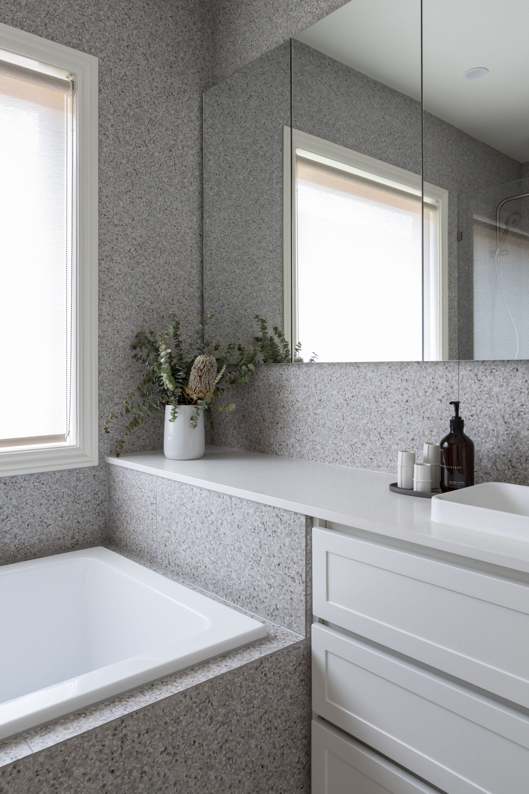 Built in bath with grey tile against a custom vanity unit with shaker style drawers in white