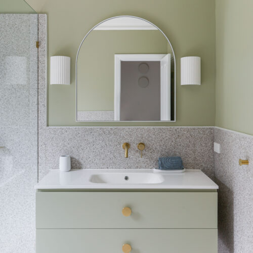 Green vanity unit with arched wall mirror against terrazzo wall tiles