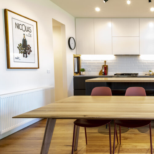 Timber dining table in front of contemporary charcoal & white kitchen